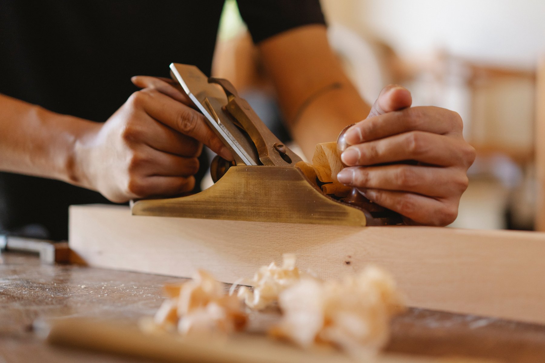 Crop man shaping wood with hand plane in workshop